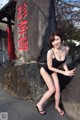 A woman in a black bathing suit posing next to a large rock.