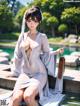 A woman in a white dress sitting on a ledge by a pool.