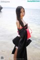 A woman in a black and red dress standing on a beach.