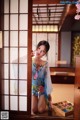 A woman in a blue kimono sitting on the floor in front of a window.