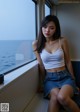 A woman sitting on a window sill looking out at the ocean.