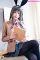 A woman in a bunny suit sitting on a desk holding a book.