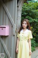 A woman in a yellow dress standing next to a pink mailbox.