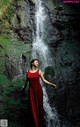 A woman in a red dress standing in front of a waterfall.