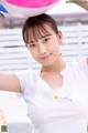 A woman in a white shirt holding a pink and blue balloon.