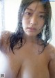 A naked woman standing in front of a window with water droplets on it.