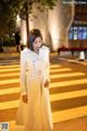 A woman in a white trench coat standing on a crosswalk.