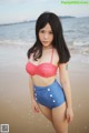 A woman in a red and white polka dot bikini top and blue shorts on the beach.