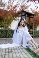 A woman in a white dress sitting on a wooden deck.